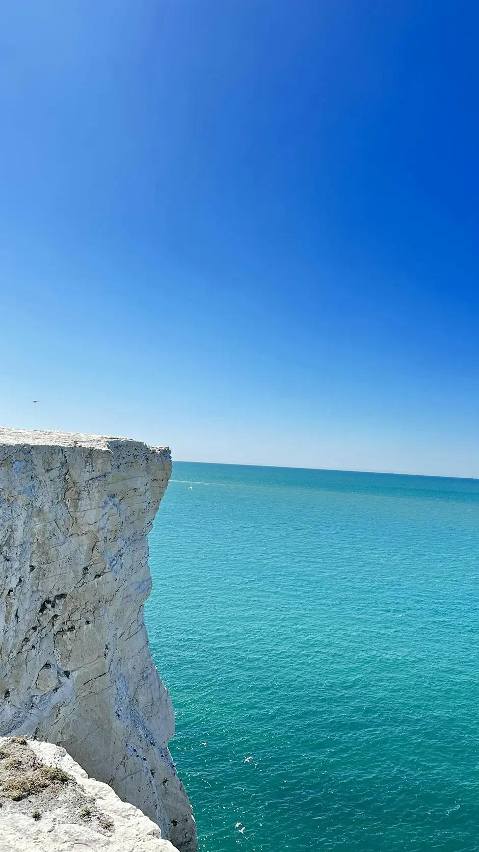 White chalk cliffs dropping into a turquoise sea under a clear blue sky.