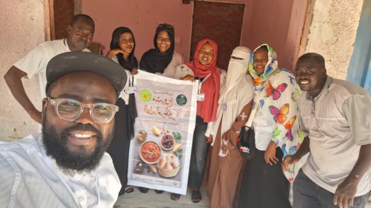 Members of the Bidaya team gathered together on distribution day, one holding the food-project poster.